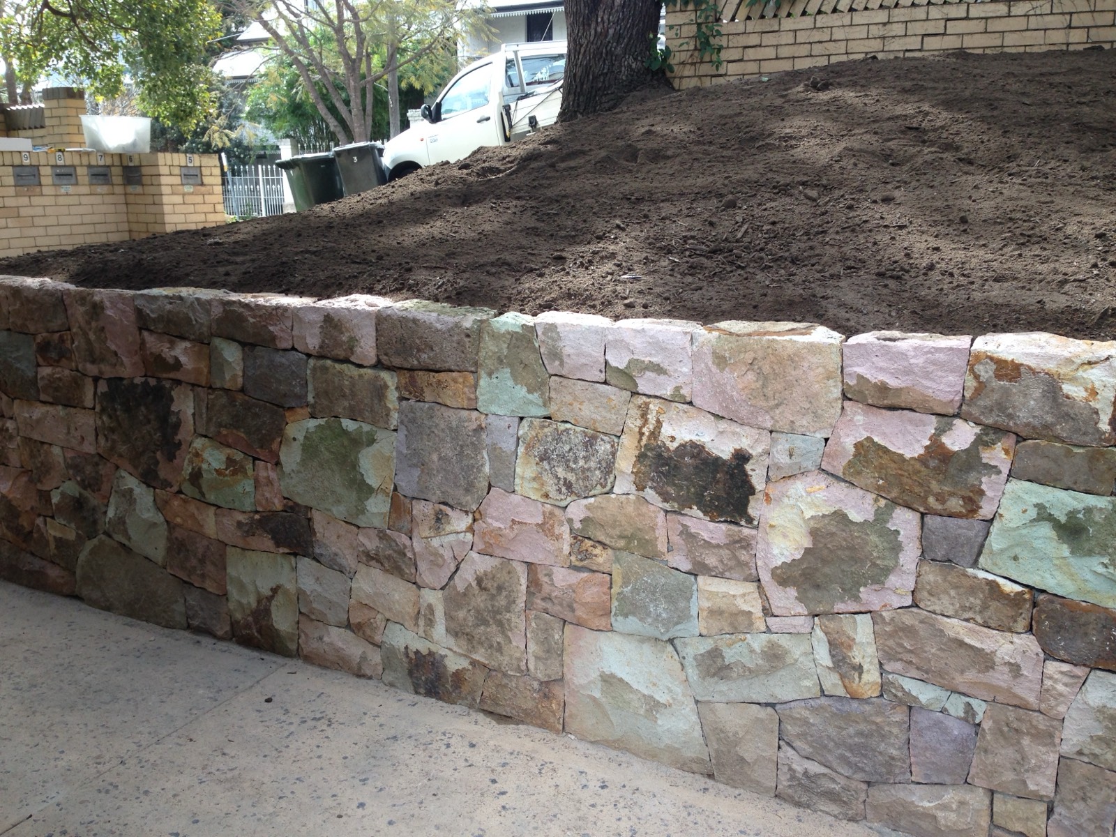 Coloured sandstone retaining wall along a footpath, freshly soiled garden above