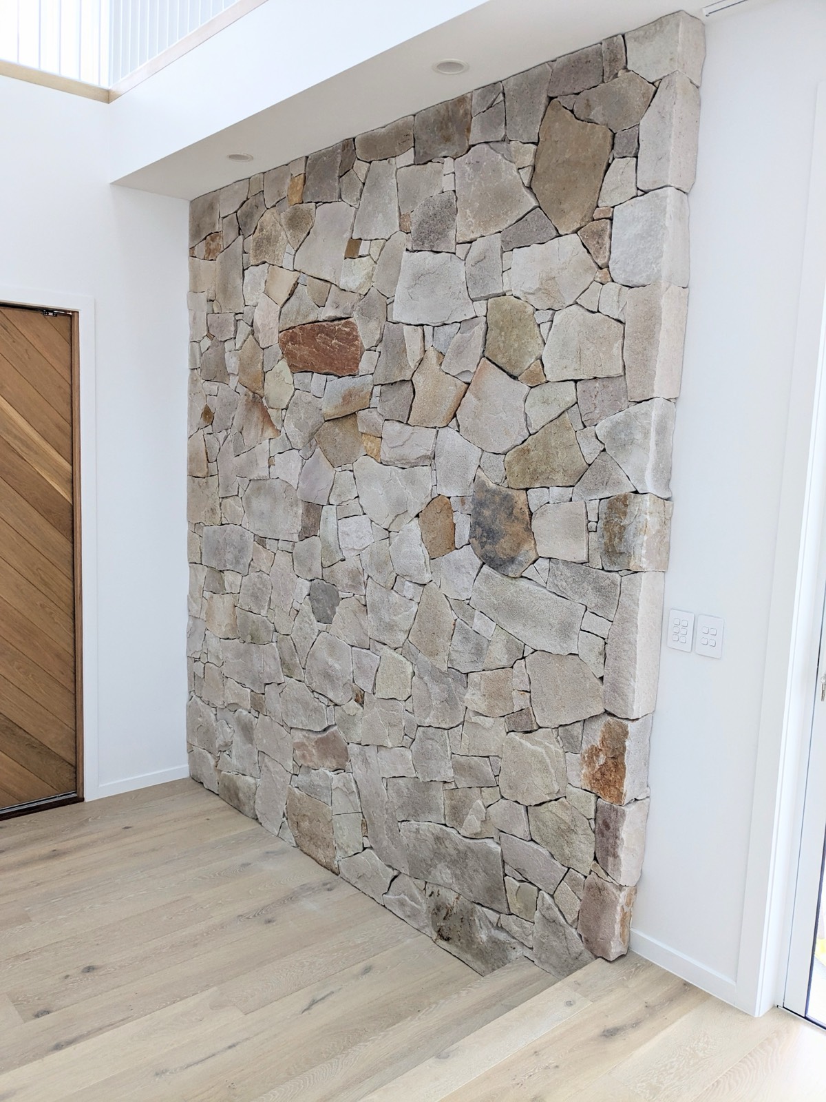 Interior random-stone feature wall beside timber door and oak floors