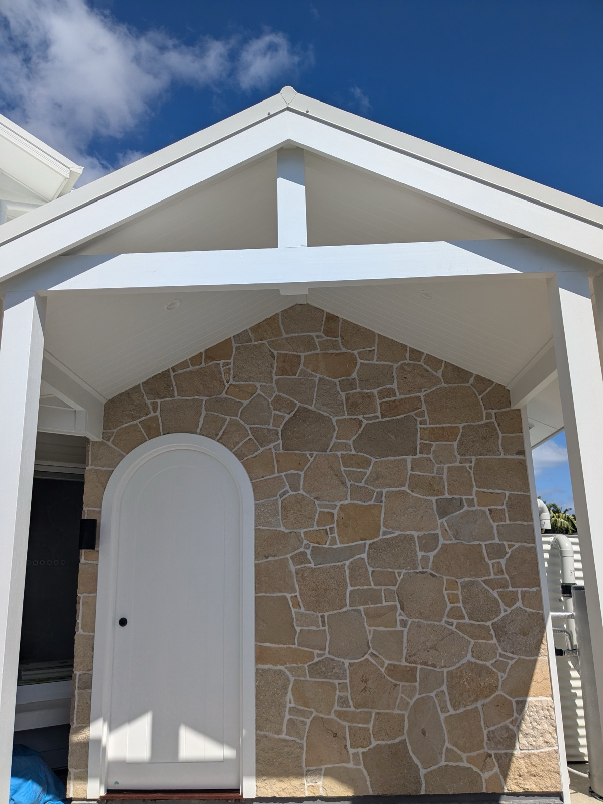 Sandstone-clad gable wall with white arched door under a new pergola